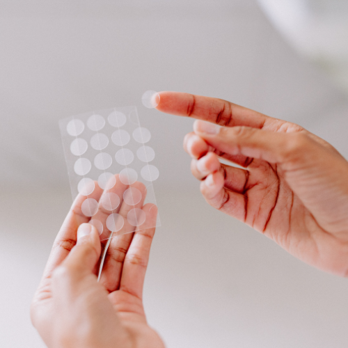 woman's hands holding sheet of transparent round pimple patch stickers