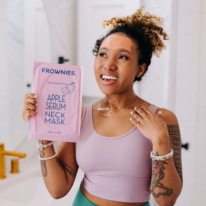 Frownies apple serum neck mask being held by a black woman with curly hair who also has it on her neck
