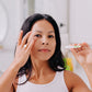 A woman with black hair shown applying Frownies apple serum to her under eye area