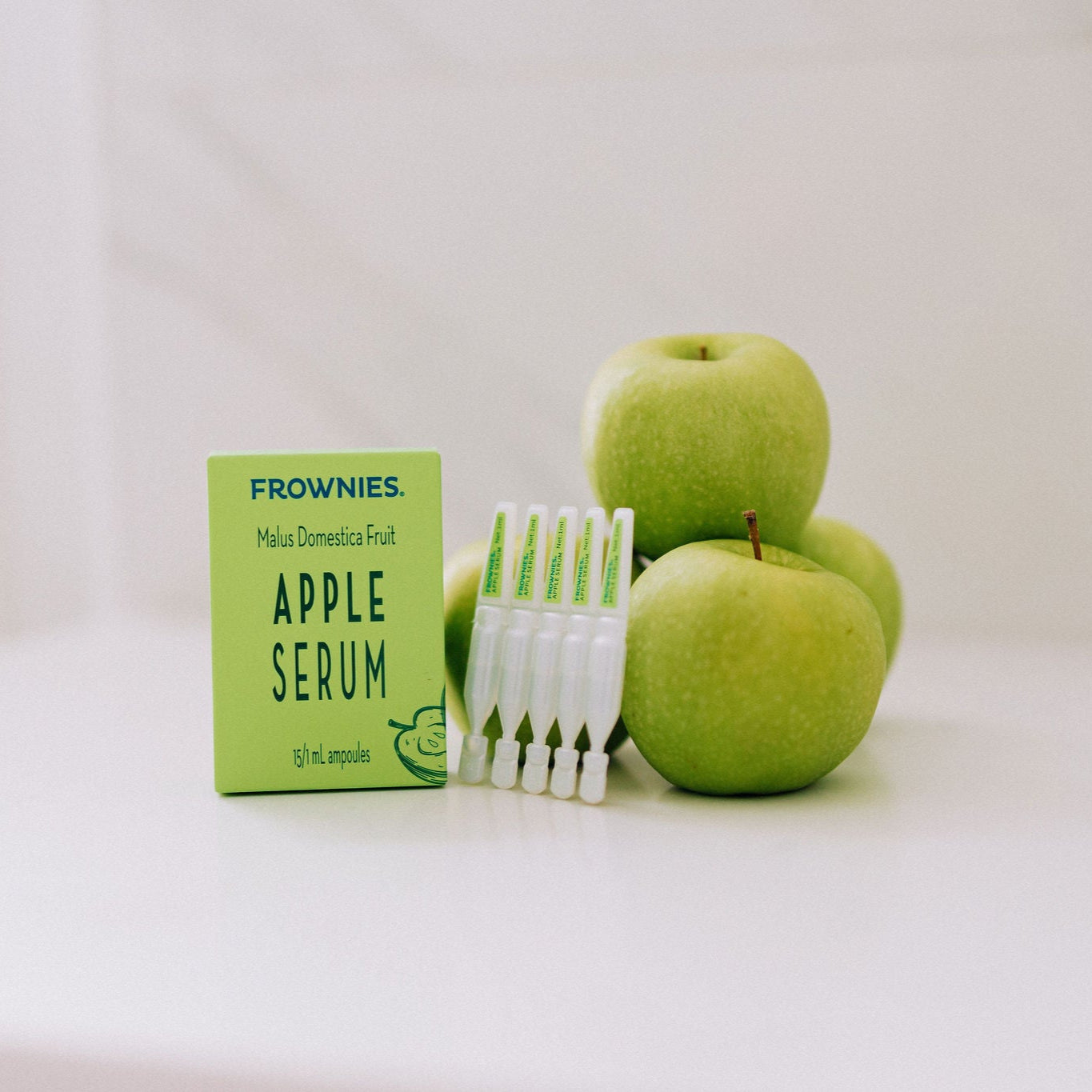 Frownies apple serum pictured next to green apples and showing what the product looks like outside the box