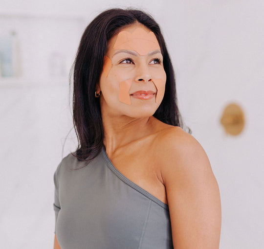A woman with black hair shown wearing Frownies facial patches. For forehead and between the eyes and corners of eyes and mouth 
