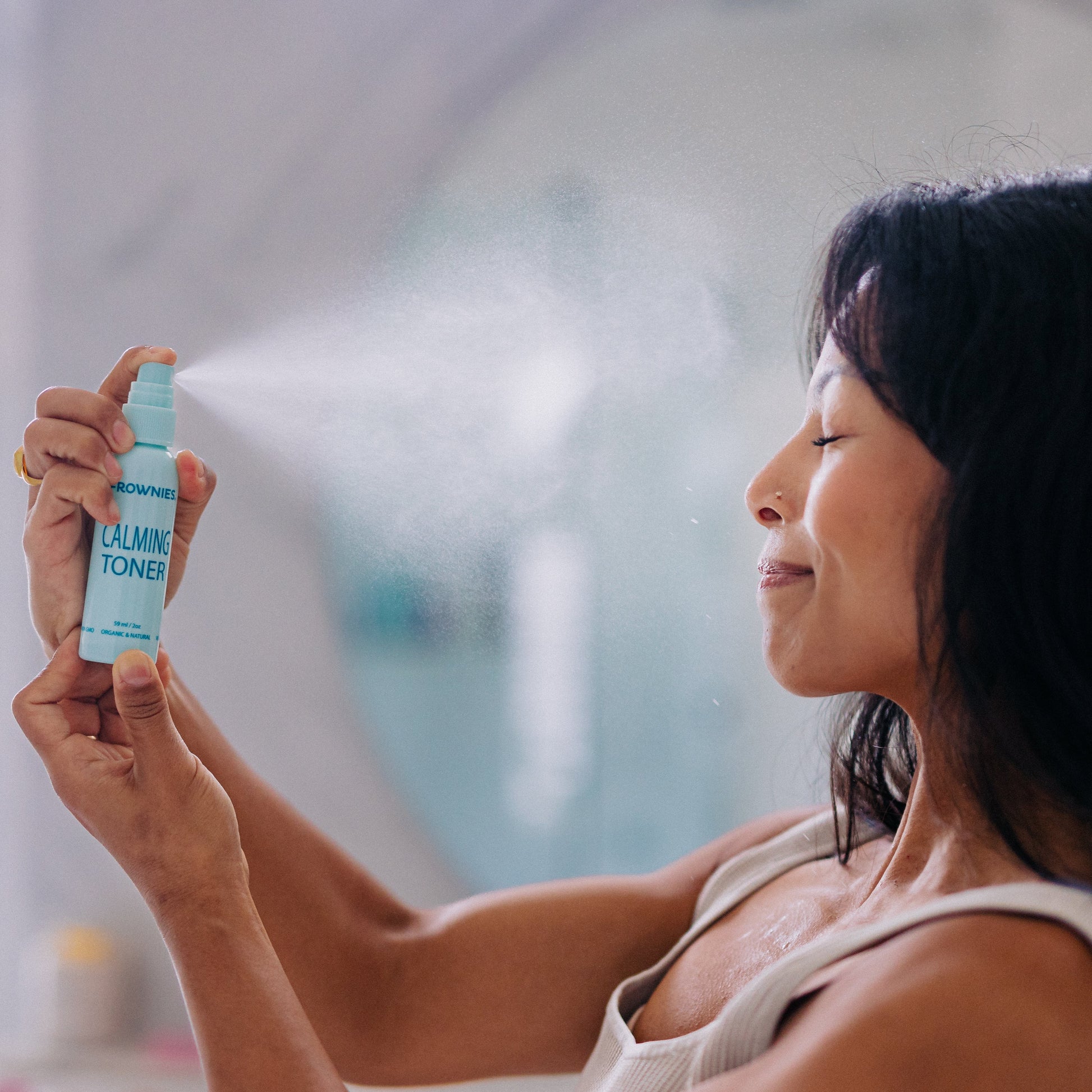 A woman spraying calming toner onto her face