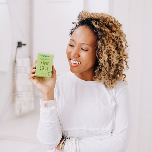 A black woman with curly hair shown holding Frownies apple serum 
