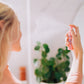 A woman with blonde hair shown spraying Frownies rose water hydrator spray onto her face. 