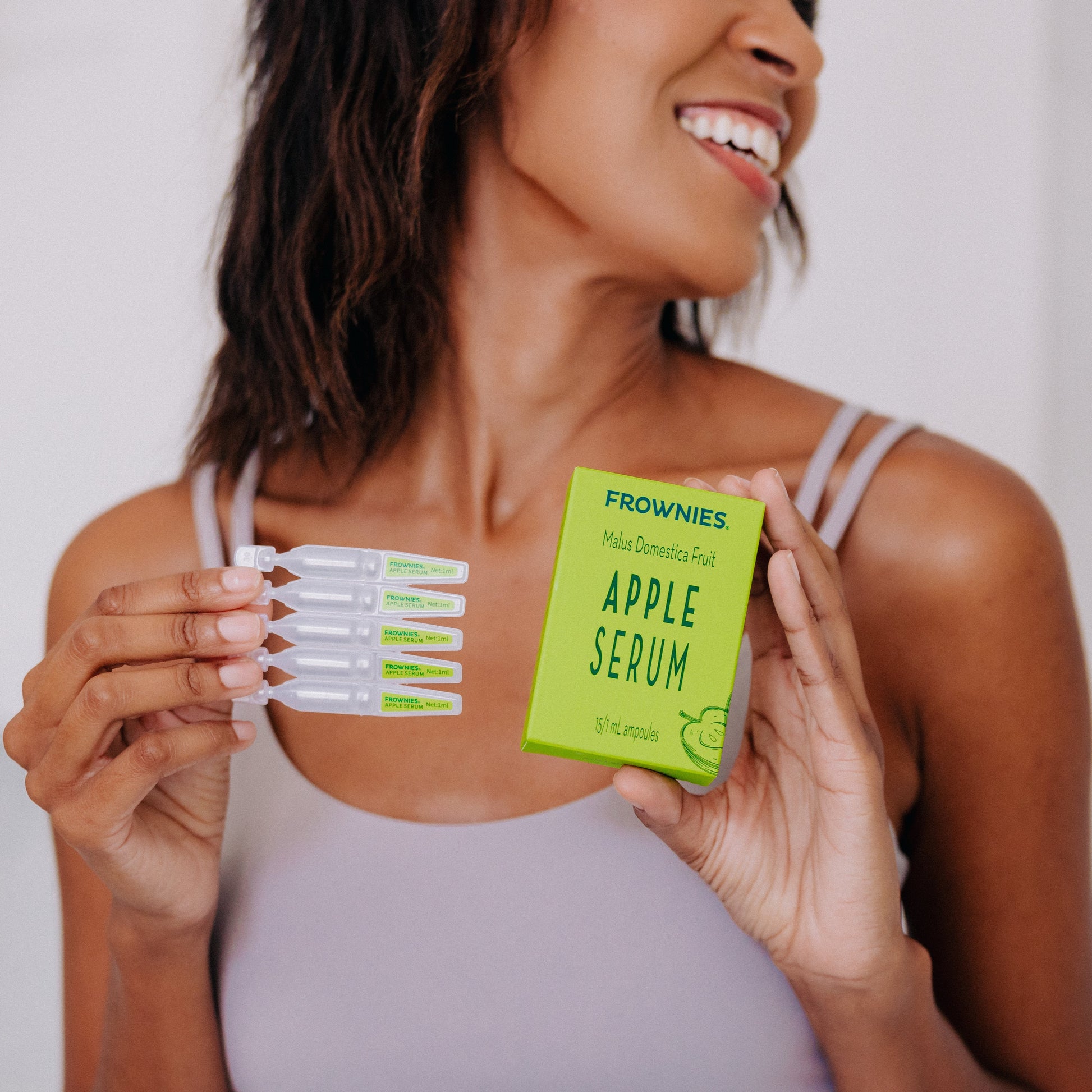 A black woman shown holding Frownies apple serum package and serum in her hands