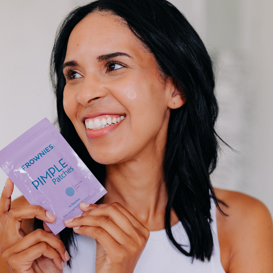smiling woman holding purple package near her face while wearing clear pimple patches