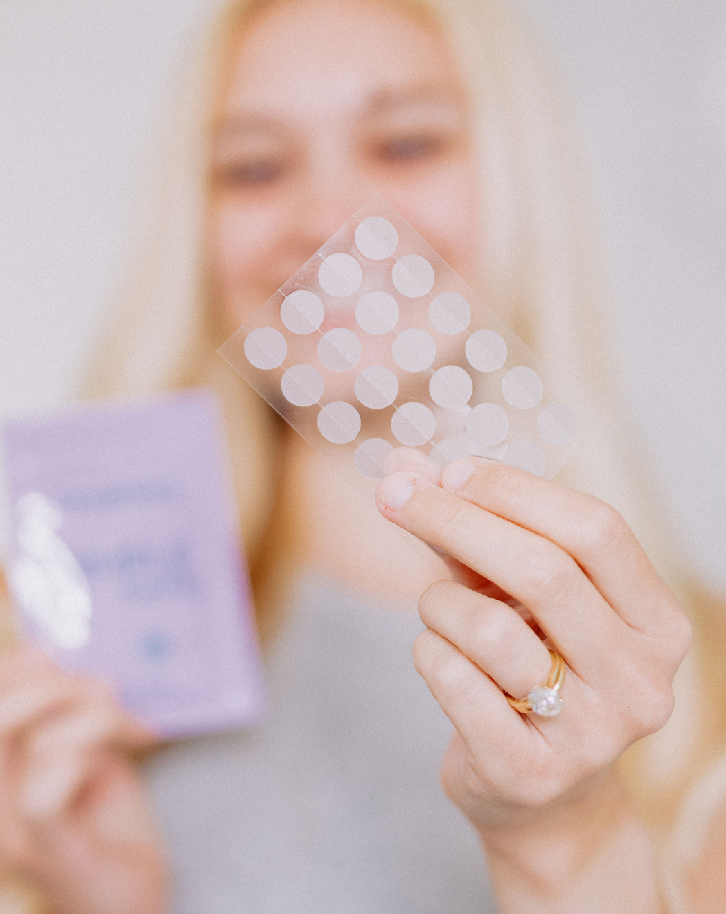 woman's hand holding clear plastic sheet of circle pimple patches