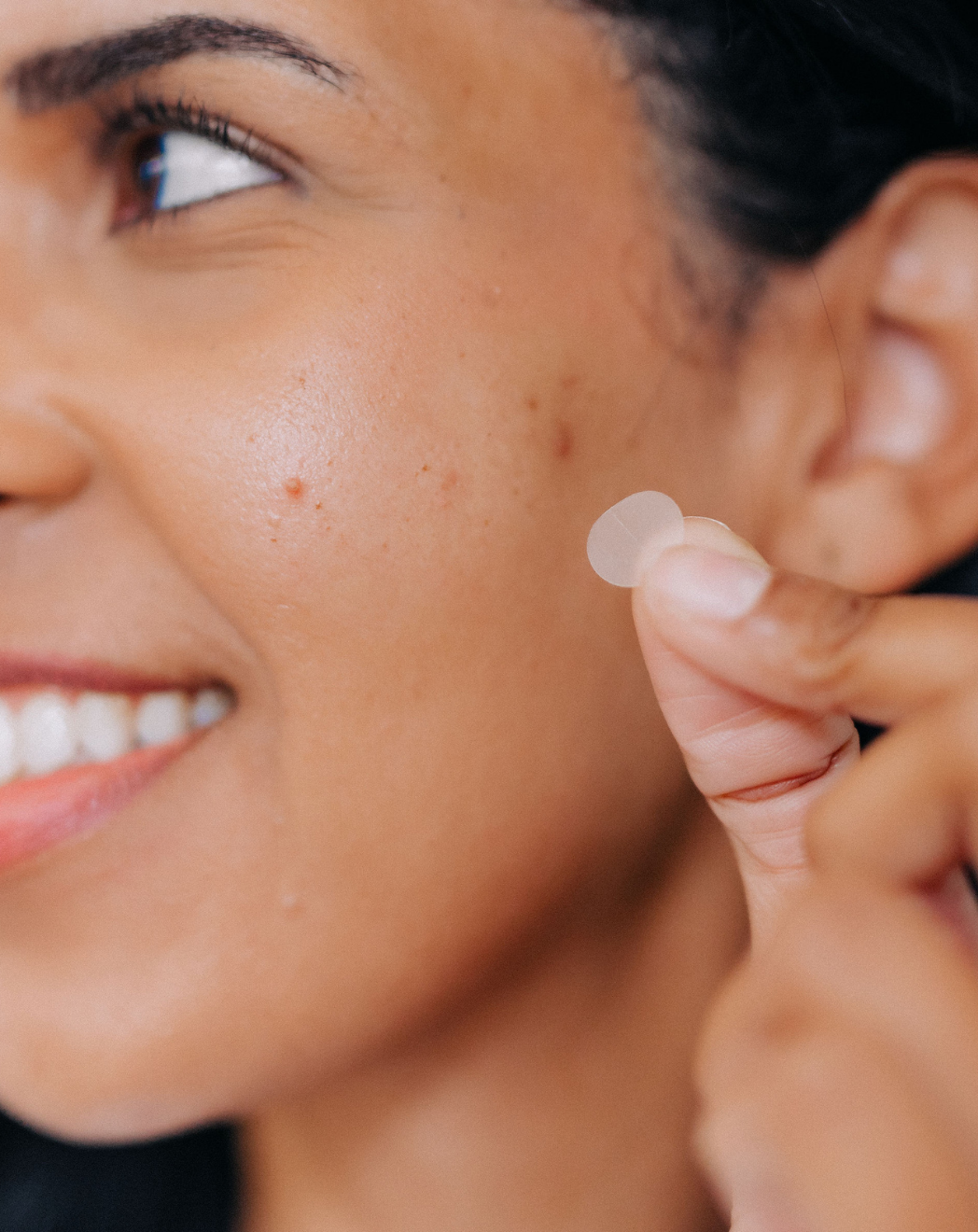 partial view of woman's face applying frownies pimple patches with essential oils 
