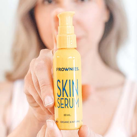 blurry woman holding in background holding up yellow bottle of Frownies Skin Serum 