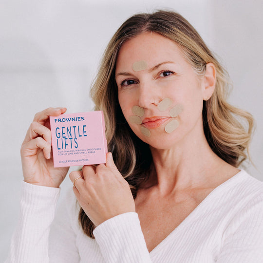 A woman with blonde hair wearing Frownies Gentle Lifts while holding up the packaging to examine it.